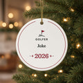 Personalized round ceramic golfer Christmas ornament with the name Jake and 2026, hanging by a gold string on a lit Christmas tree